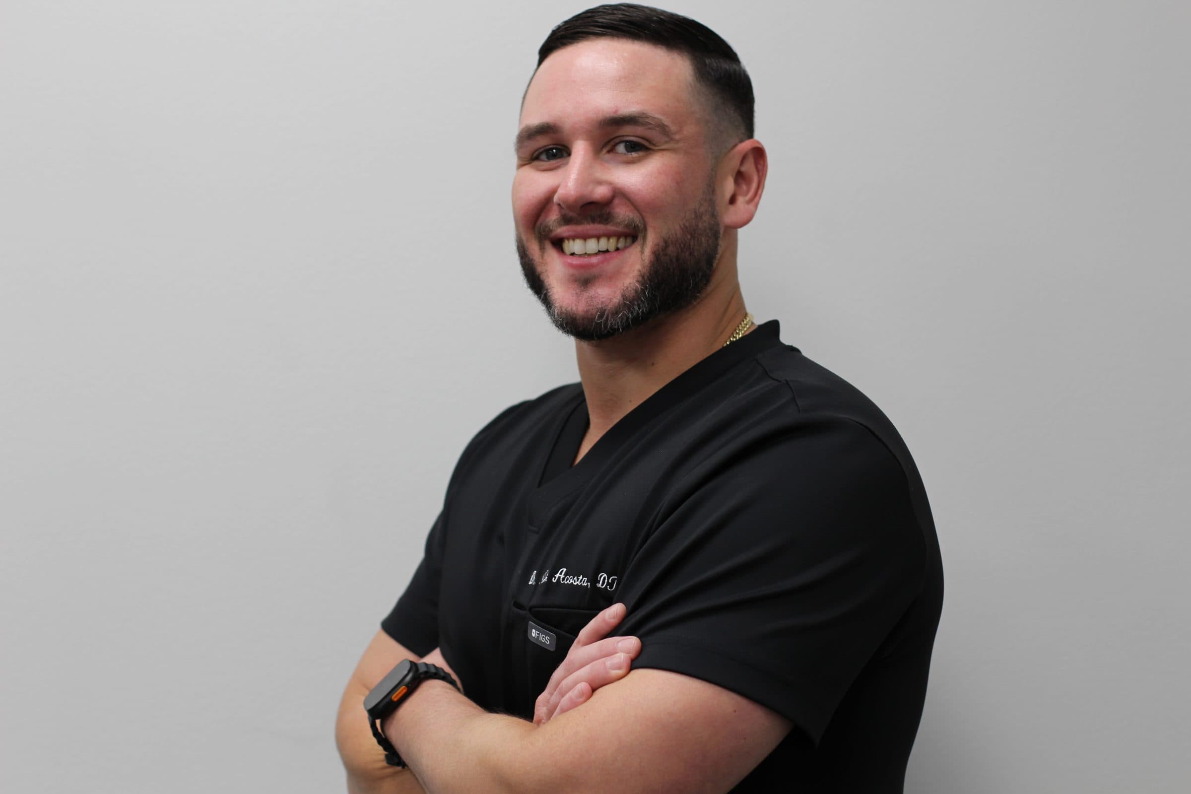 Dr. Nicholas Acosta in black scrubs, arms crossed, smiling